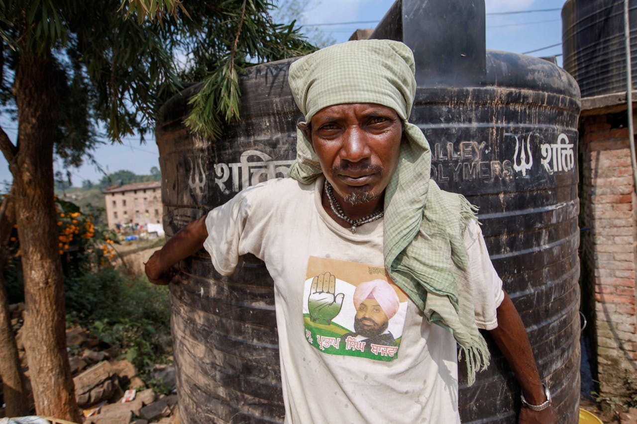 Portrait of a rural man wearing a headscarf standing outdoors by a water tank.