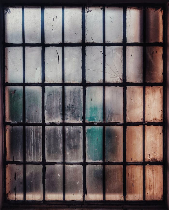gallery-1 A weathered and dirty glass window with a rusty frame, featuring textured panes and a vintage look.